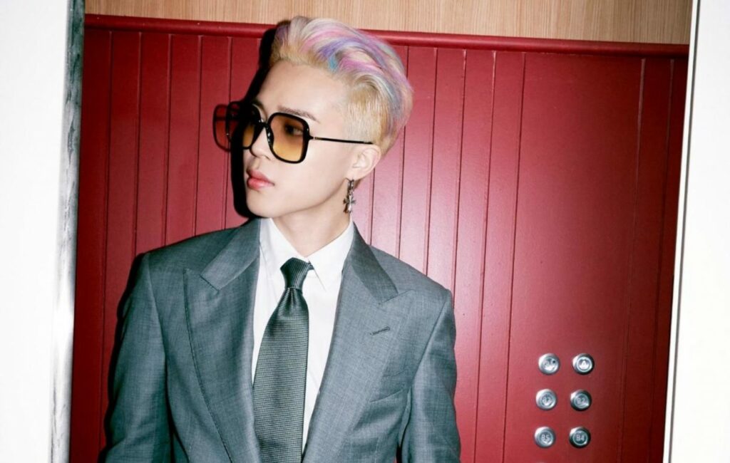 BTS' Jimin wearing a suit and sunglasses poses by a red door