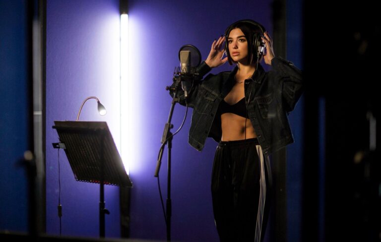 Dua Lipa pictured wearing headphones by a mic in a studio