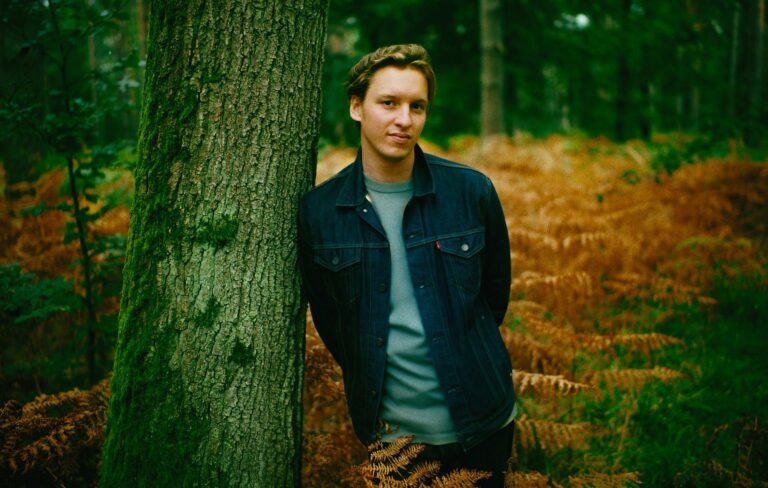 George Ezra is seen leaning against a tree in a press shot