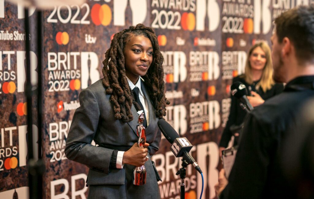 Little Simz poses on the BRIT Awards 2022 red carpet while holding her award