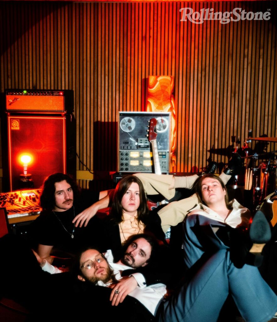 Blossoms pose as a group in a studio under a red tinged light