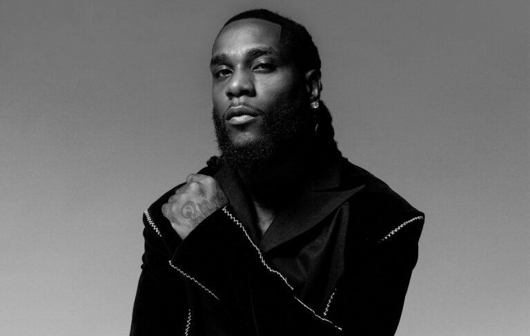 Burna Boy wears a black jacket and diamond earring, posing for Rolling Stone UK in a black and white shot