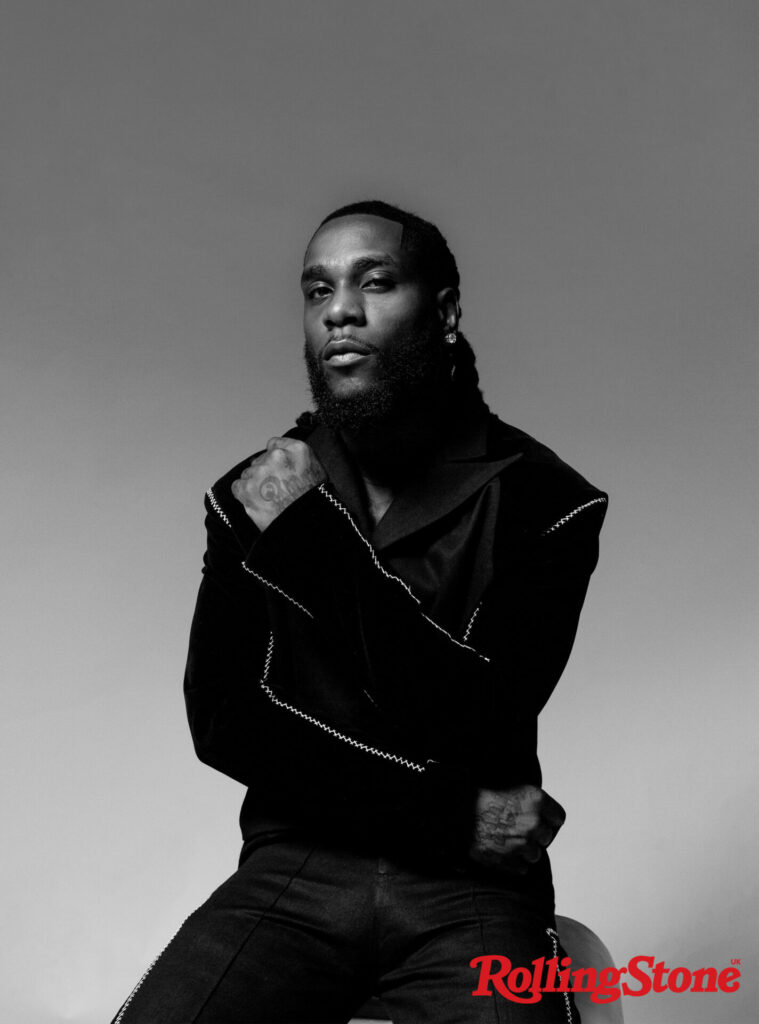 Burna Boy wears a black jacket and diamond earring, posing for Rolling Stone UK in a black and white shot