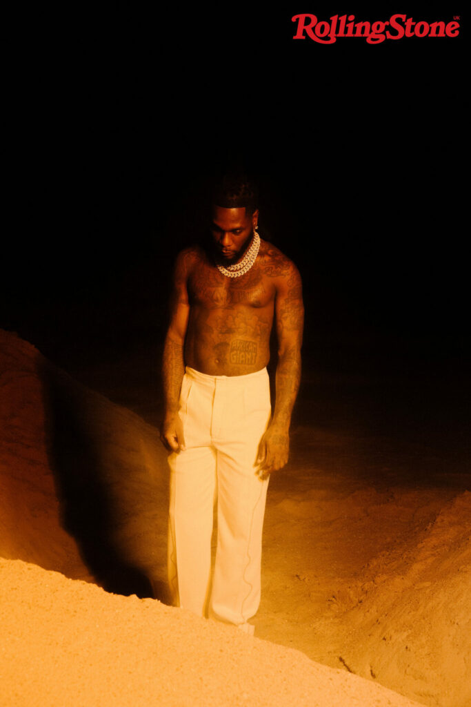 Burna Boy poses shirtless in white trousers and wears a thick diamond chain