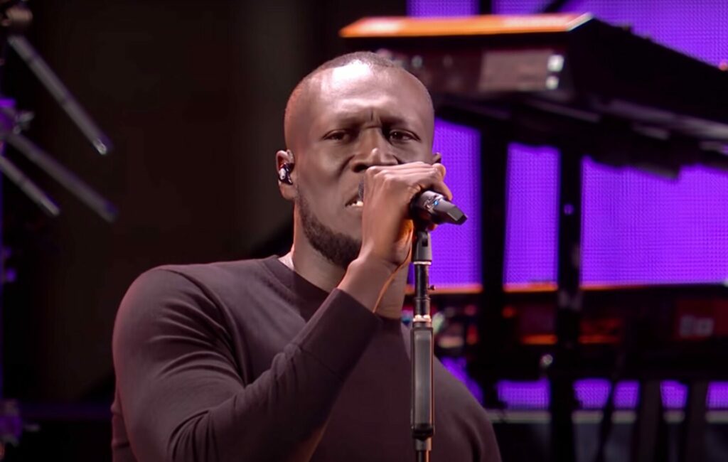 Stormzy performs live in front of a microphone in a black shirt