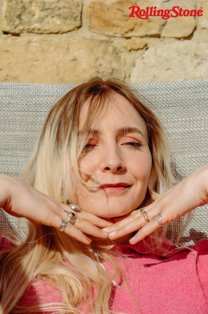 Hester from Wet Leg poses for a headshot with her hands underneath her chin covered in rings