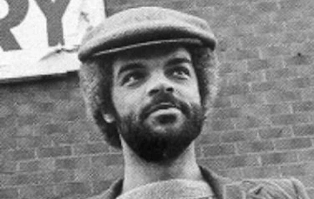 Alan Erasmus poses in a black-and-white photo wearing a flat cap