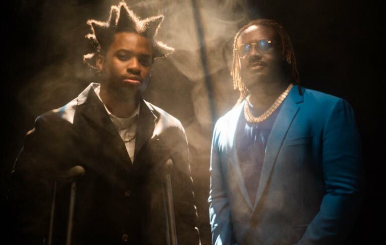 Denzel Curry and T-Pain pose for a music video in a smoky room