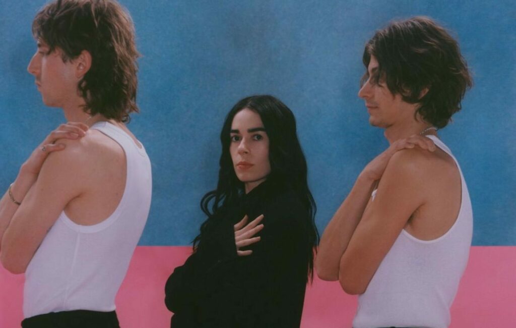 Sinead O'Brien stands in between two men against a pink and blue backdrop