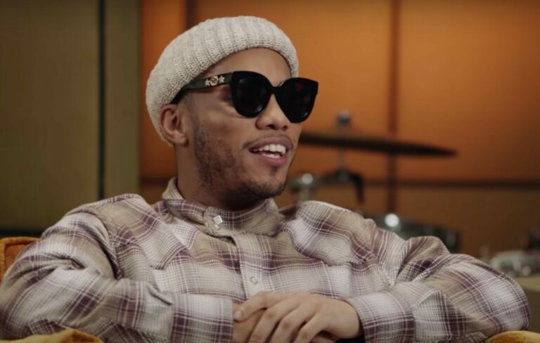 Anderson .Paak wears a beanie hat, sunglasses and checkered shirt in an interview