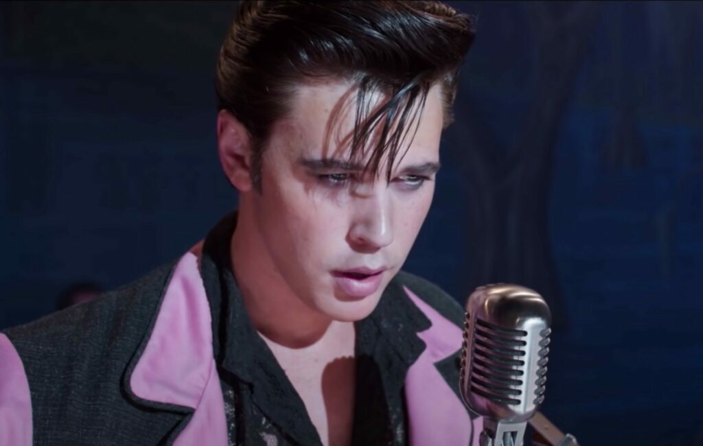 Austin Butler wears a pink and black suit and sings in front of a microphone as Elvis