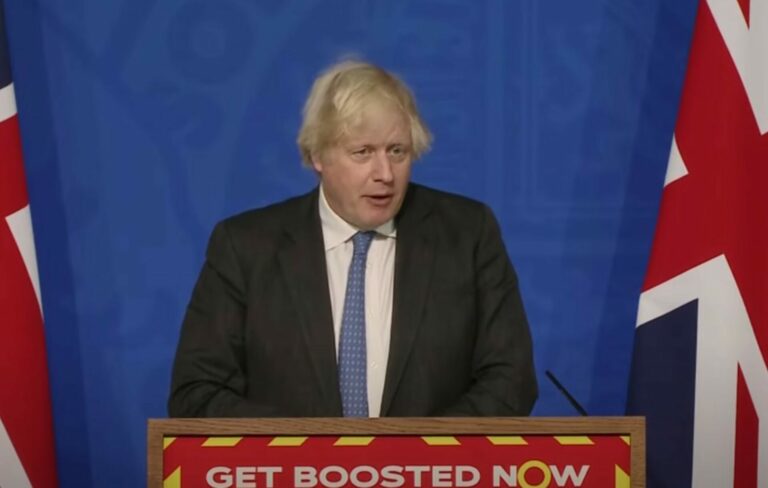 Boris Johnson wears a suit and stands at a lectern during a press conference