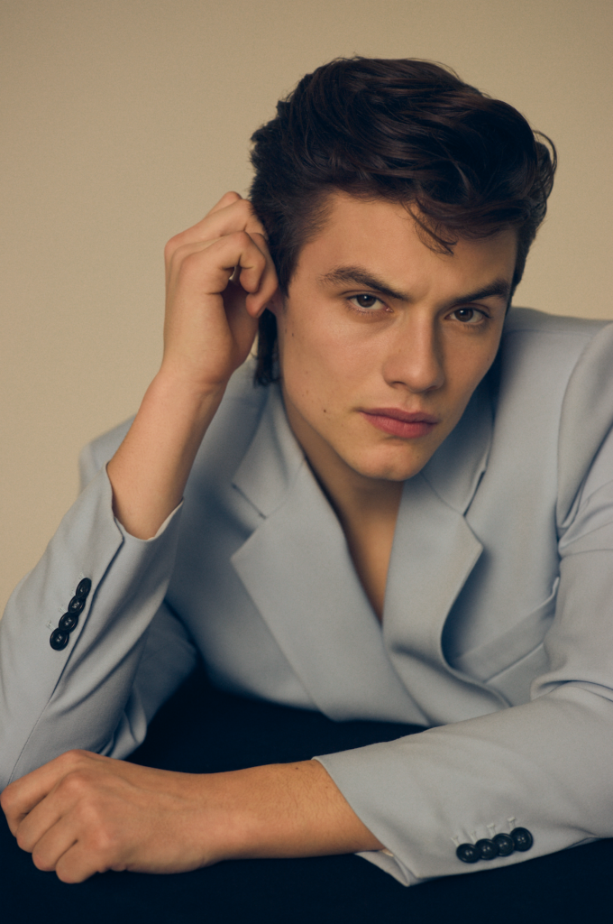 Louis Partridge wears a baby blue suit and holds his face in a headshot