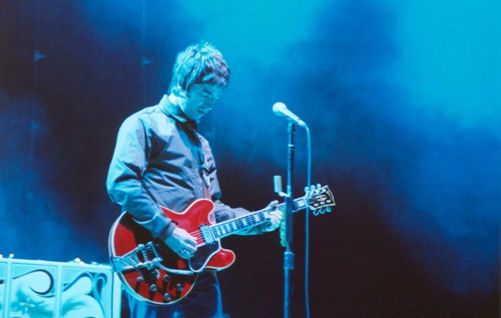 Noel Gallagher plays a red Gibson guitar on stage on 2005