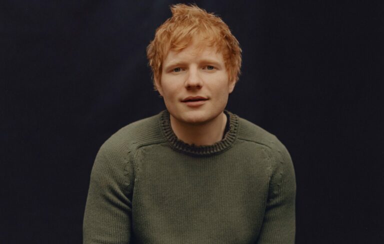 Ed Sheeran wears a grey woolly jumper against a black background