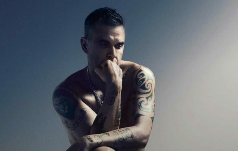 Robbie Williams poses topless with his fit at his mouth