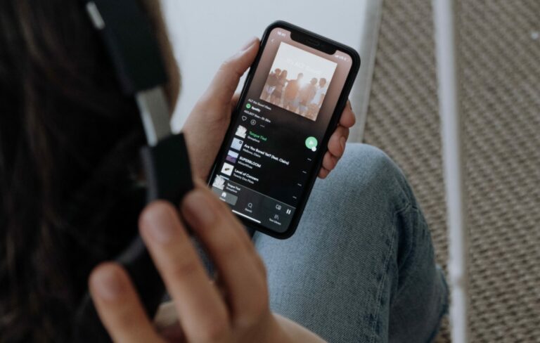 A man wearing headphones looks at the Spotify app on his phone