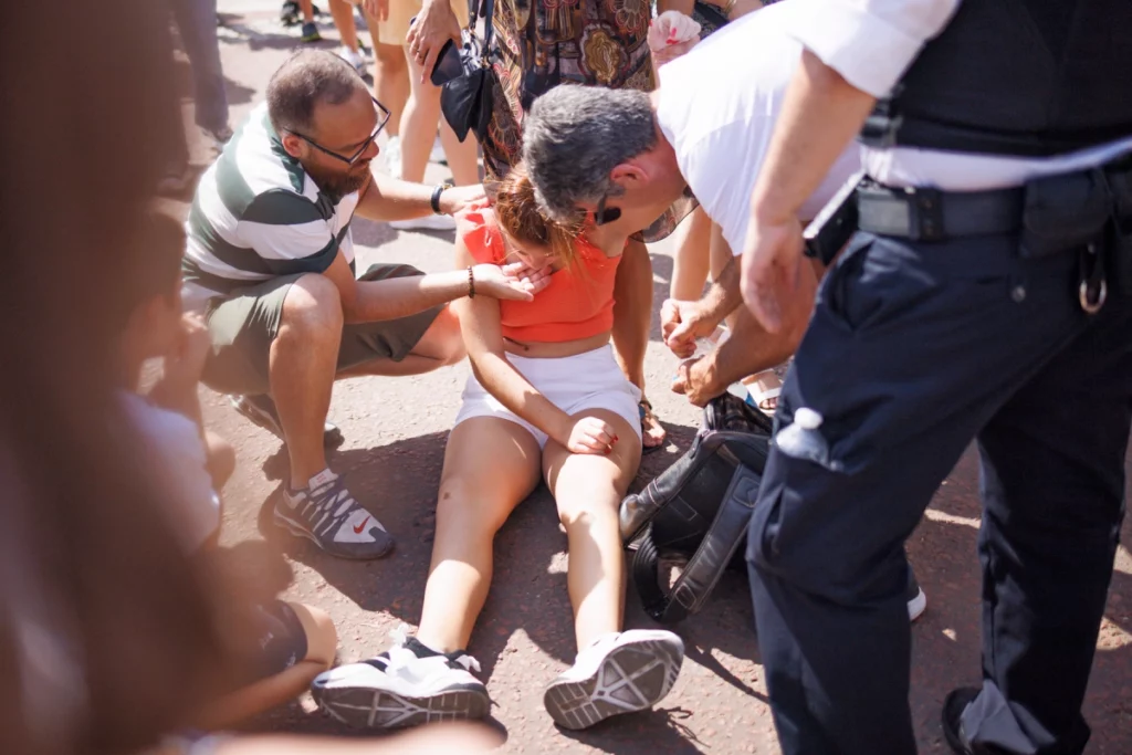 Members of the public attend to a woman who fainted in the intense heat, outside Buckingham Palace in Westminster on July 19th, 2022.