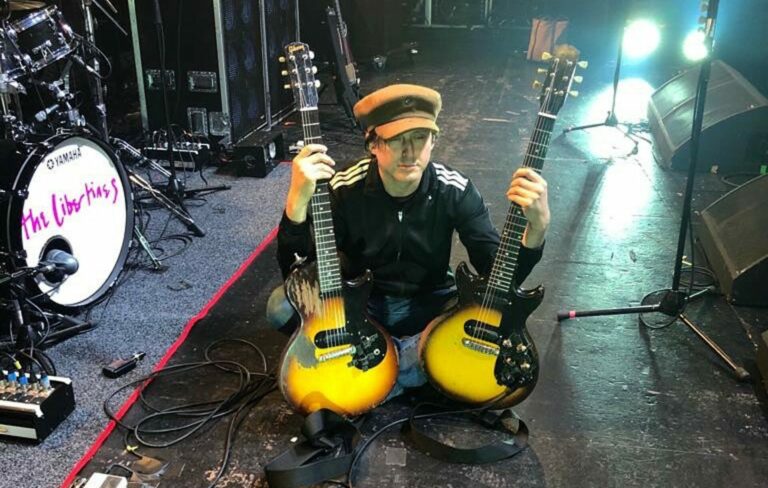 Carl Barât poses in the middle of two guitars on a stage