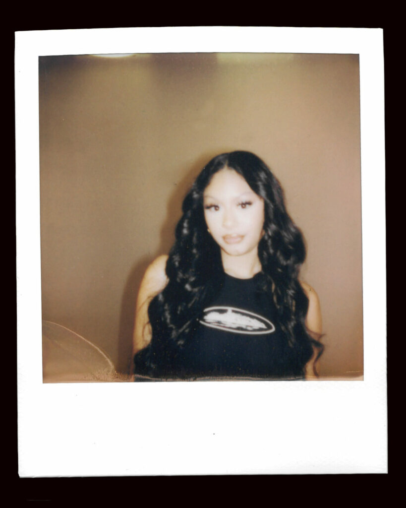 FLO's Jorja Dougla poses for a polaroid wearing a black short-sleeved top