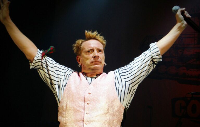 John Lydon is seen wearing a striped shirt and waistcoat