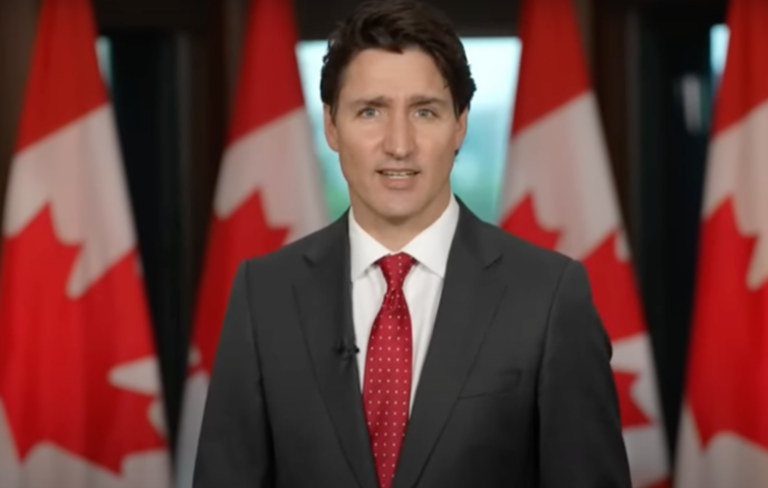 Justin Trudeau stands in front of the Canadian flags