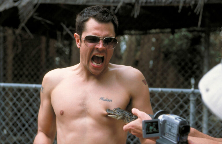 A shirtless Johnny Knoxville being bitten on the nipple by a baby alligator