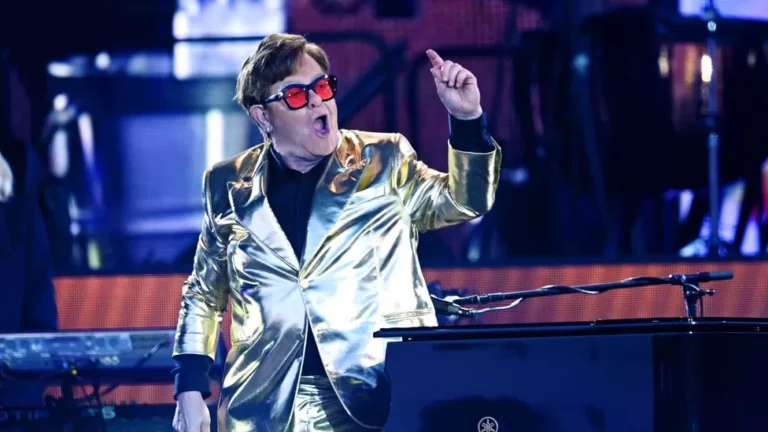 Elton John wearing a gold jacket and red lens glasses