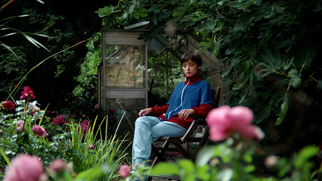 Angela Bundalovic, Miu in ‘Copenhagen Cowbody‘, sits on a bench surrounded by greenery