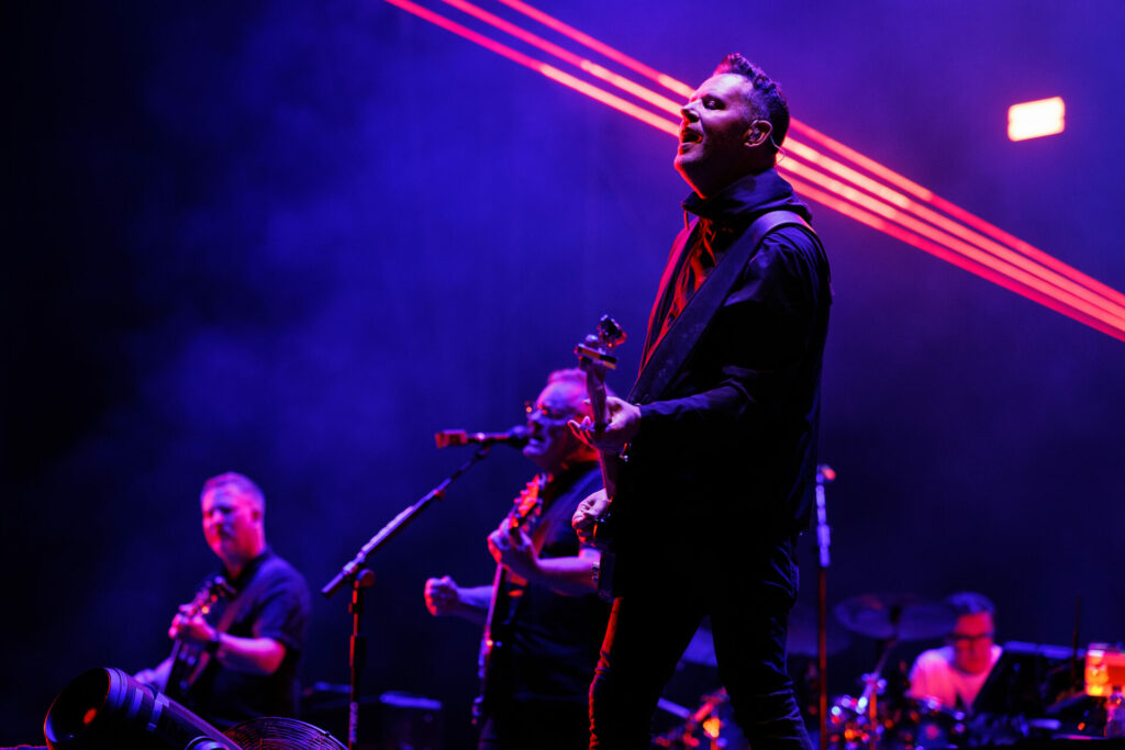 New Order perform on a stage lit with purple lights