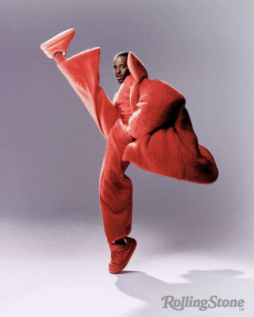 Ncuti Gatwa high kicks the air in a devil-esque red suit and jacket