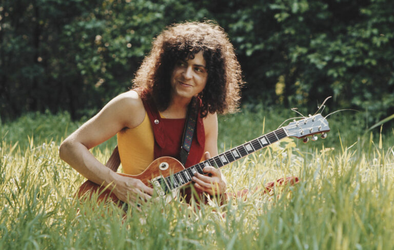 Marc Bolan of T. Rex sits in grass playing an electric guitar