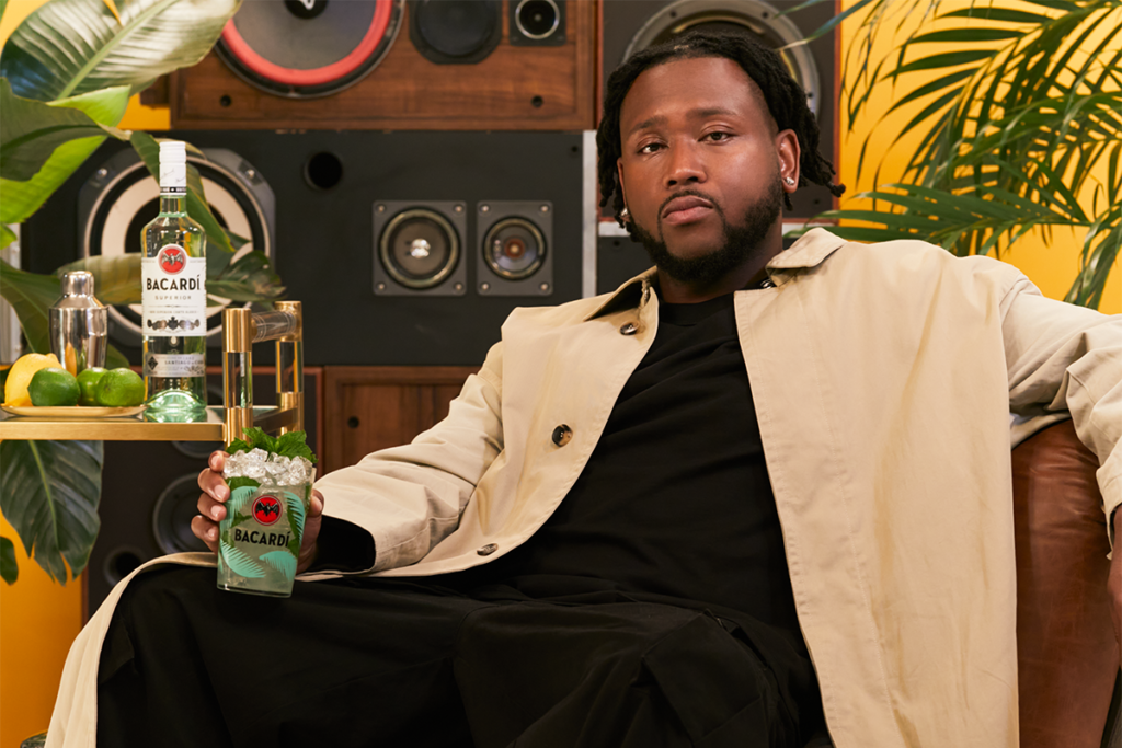 Boi-1da sits on a couch holding a bottle of Bacardi