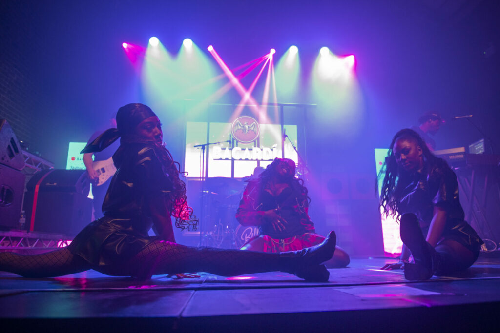 Bellah performs on stage with two dancers, one is doing a split