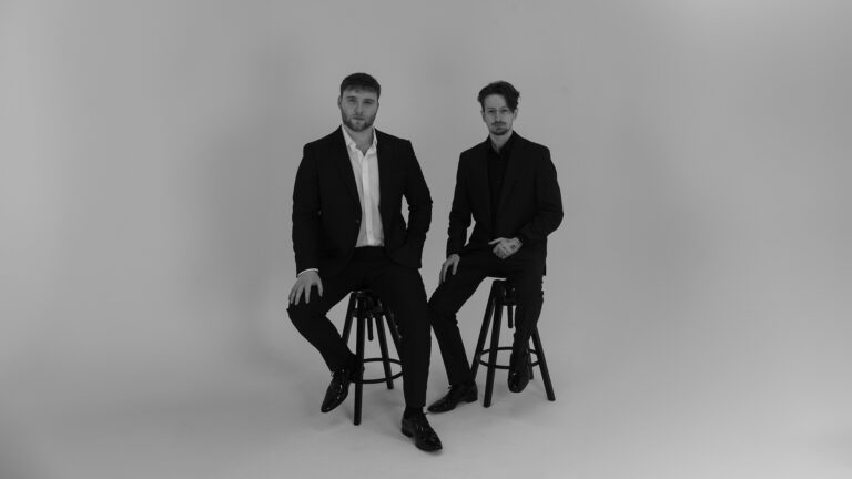 Black and white image of two men sitting on stools