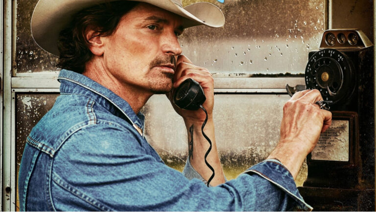Close crop of a man in a cowboy hat wearing a blue denim jacket using a payphone