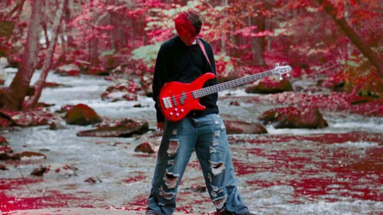 Musician Skars plays a red guitar in a forest surrounded by red foliage
