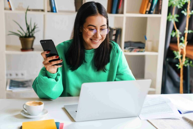 A girl in a green jumper looks into a laptop smiling