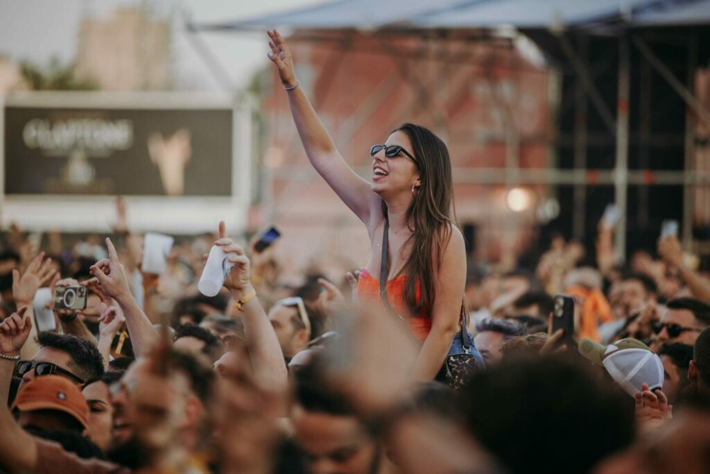 A woman sits on someone's shoulders in a crowded festival