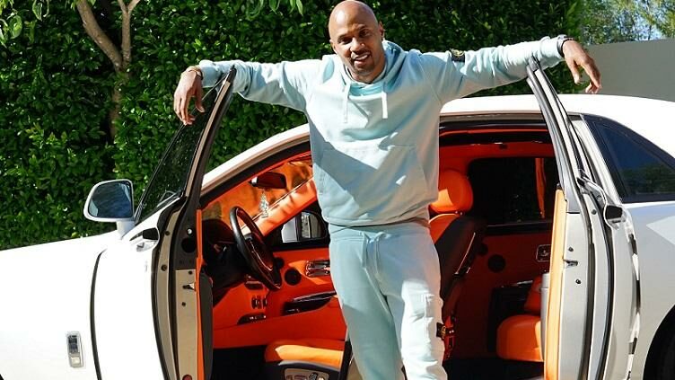 A man in a tracksuit stands in front of an open car