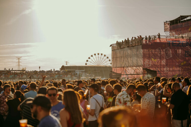 Crowded festival at dusk with a ferris wheel in the background