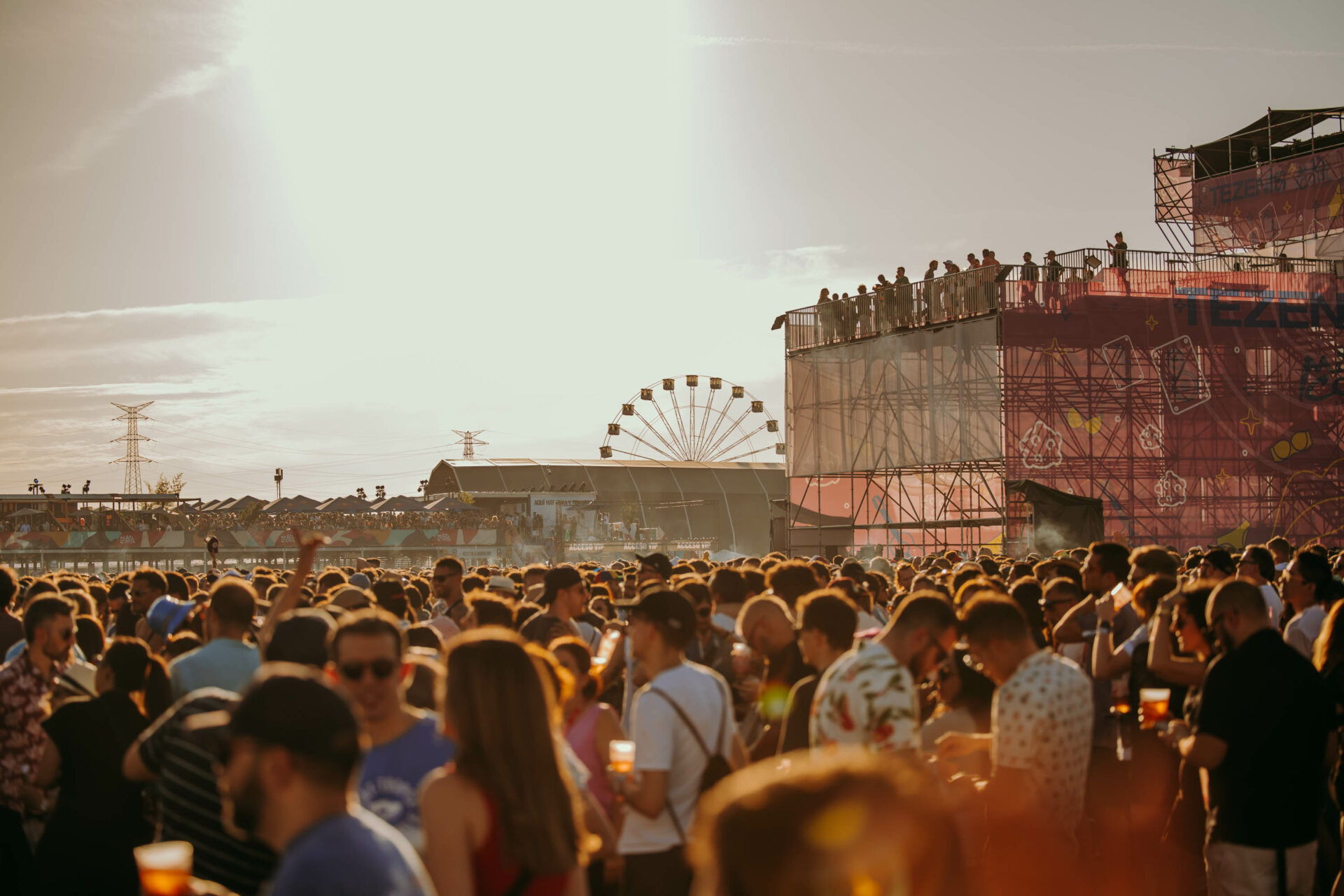 Crowded festival at dusk with a ferris wheel in the background