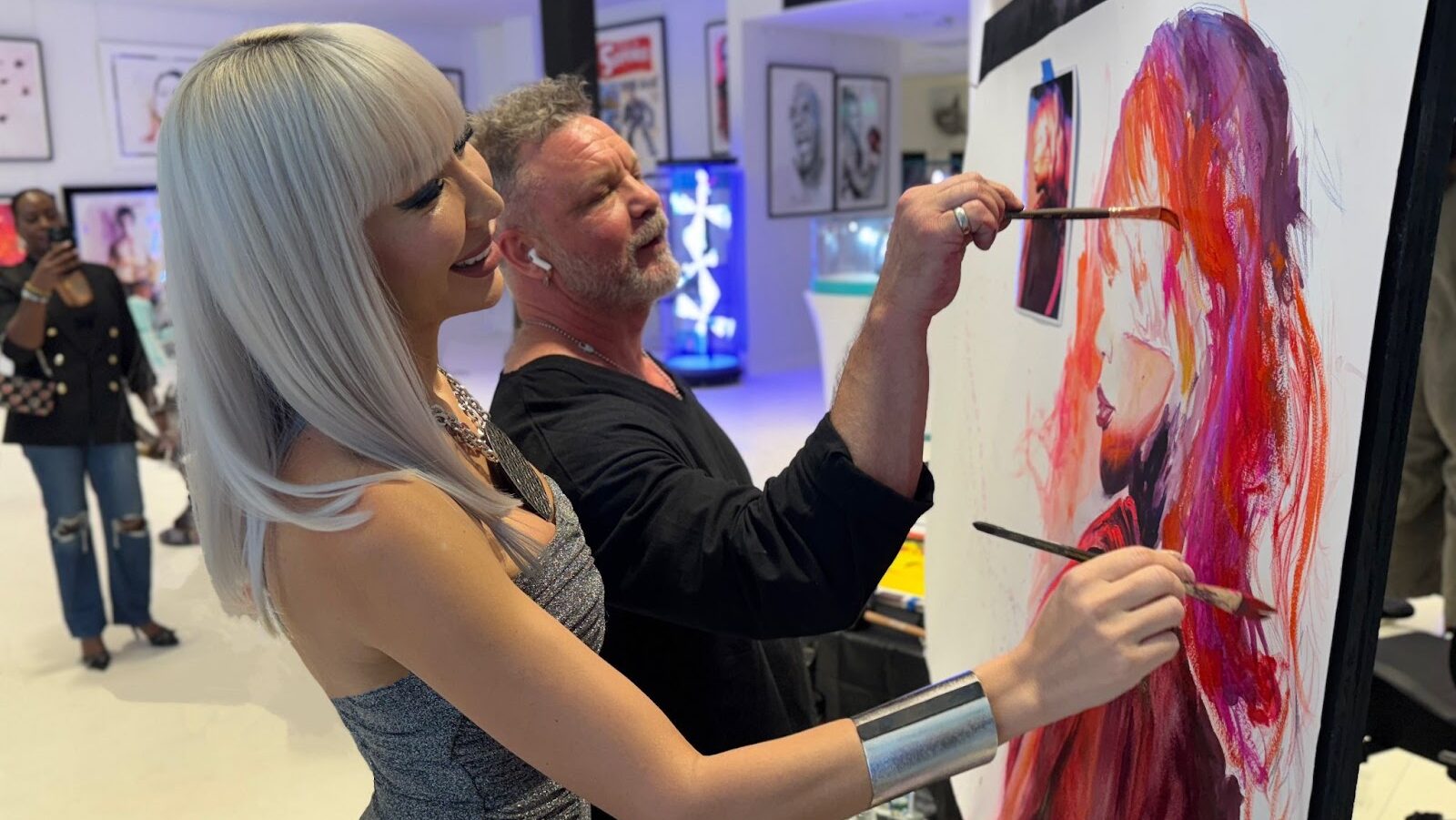Two people painting together on a large canvas at an art event.