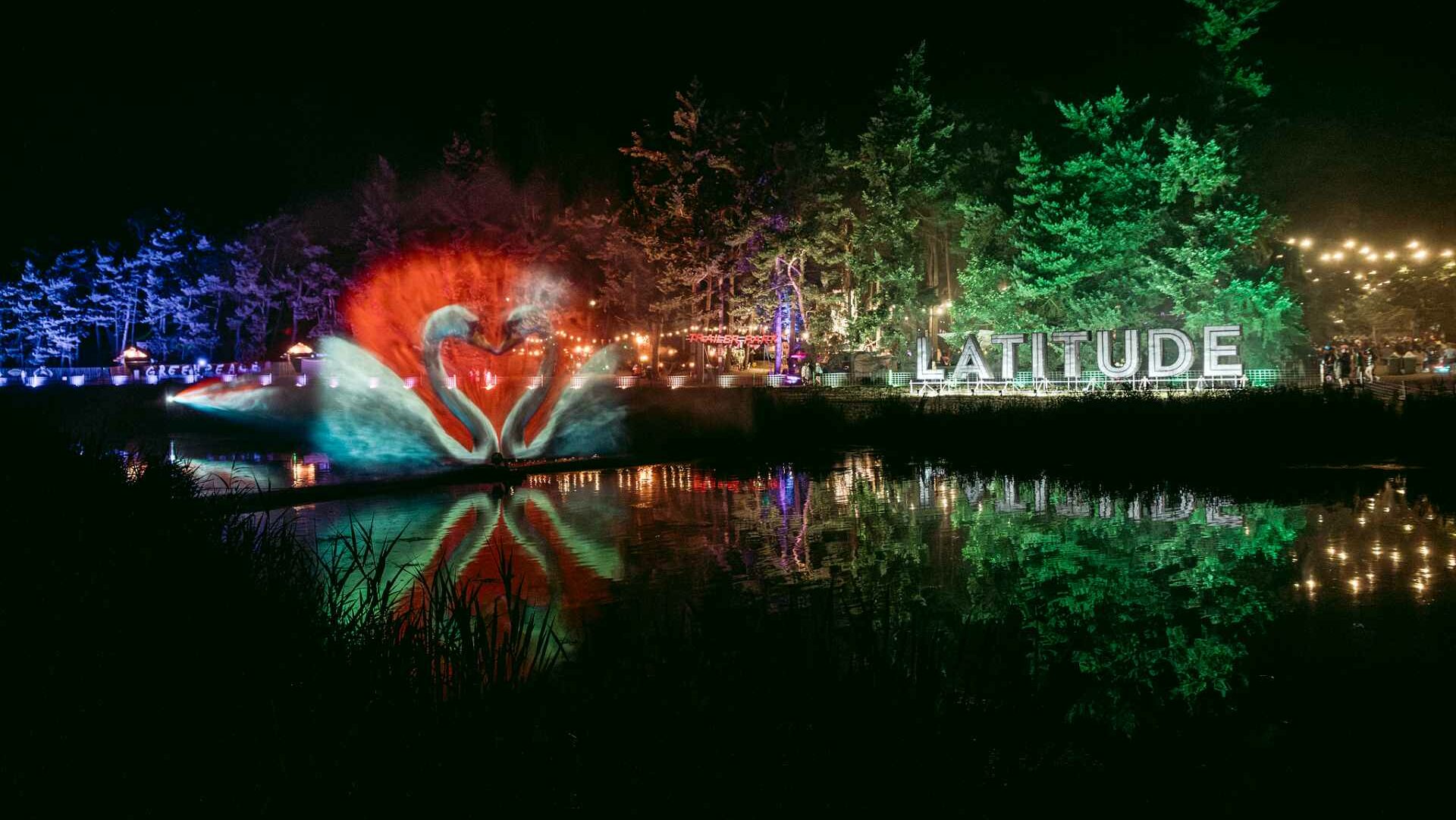 Latitude Festival sign lit up at night with colourful lights reflected in water