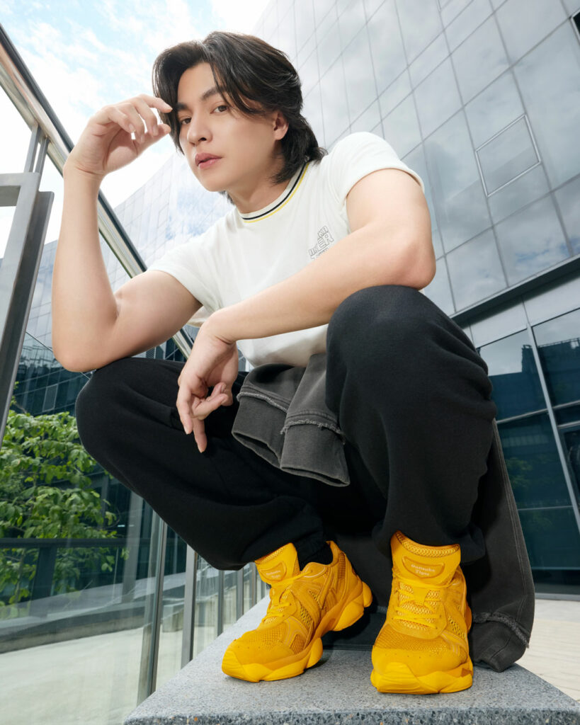 Onitsuka Tiger brand ambassador Gulf Kanawut crouching in a white t-shirt, black joggers and his all yellow TIGRUN trainers.