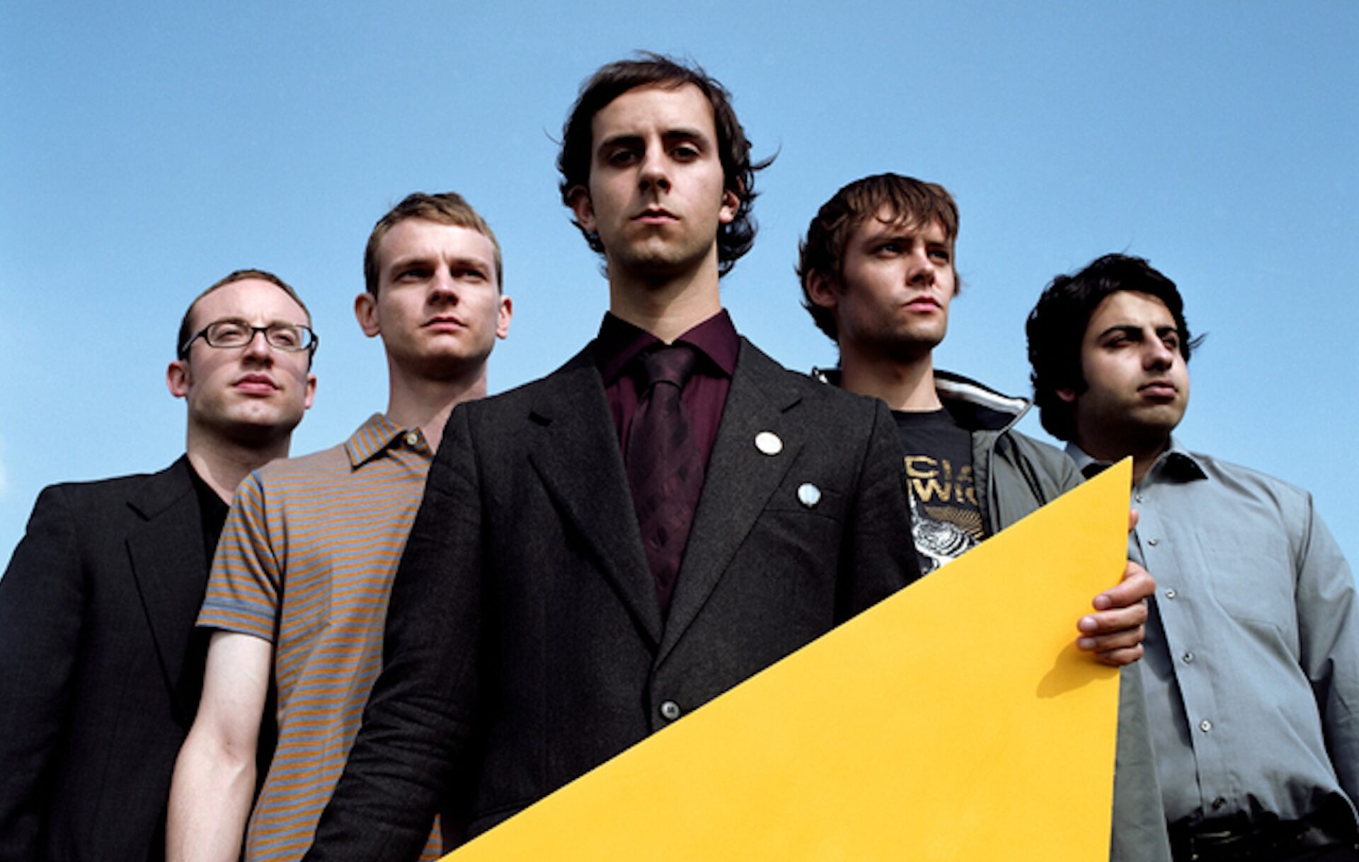 The members of Maximo Park looking down at the camera in front of a blue sky