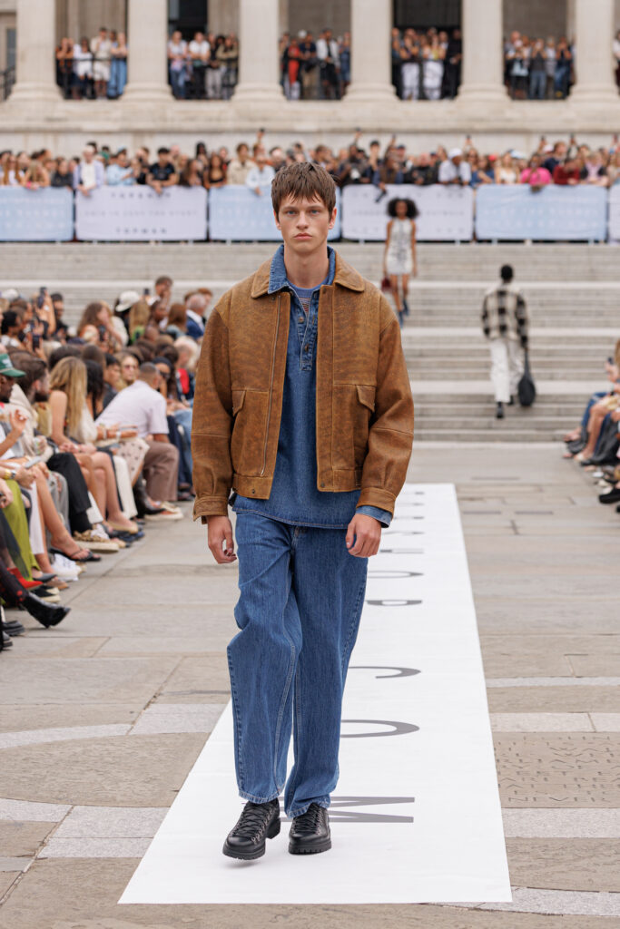 A model wearing a brown leather jacket layered over matching denim shirt and trousers walks the Topman autumn/winter 2025 show in Trafalgar Square.