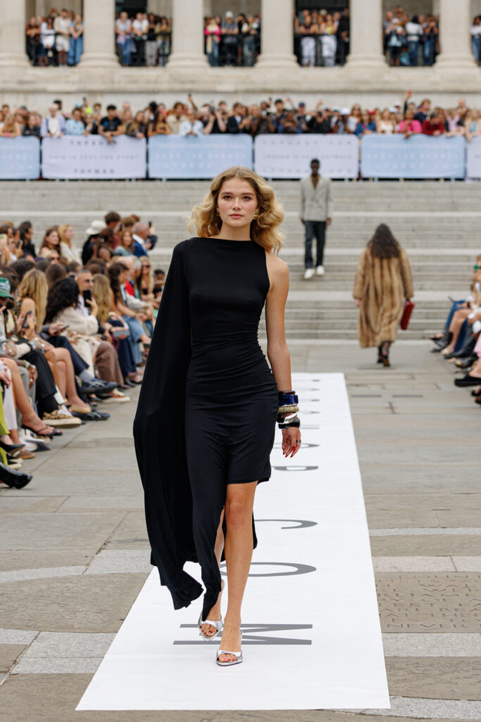 A model wearing a black asymmetric cocktail dress walks the Topshop autumn/winter 2025 show in Trafalgar Square.