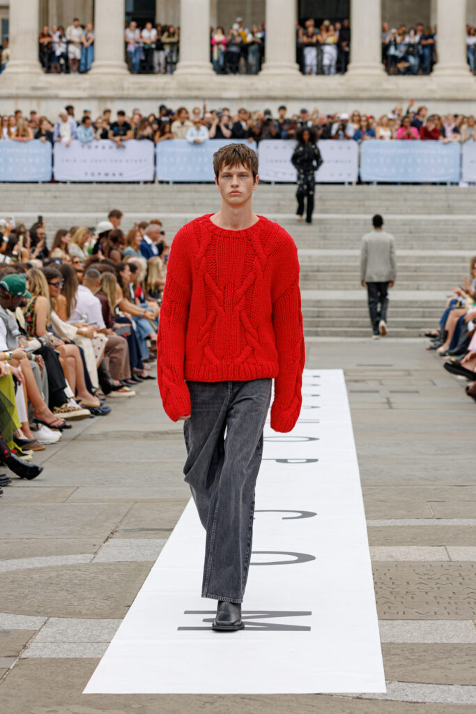A model wearing a chunky bright red knit and great trousers walks the Topman autumn/winter 2025 show in Trafalgar Square.
