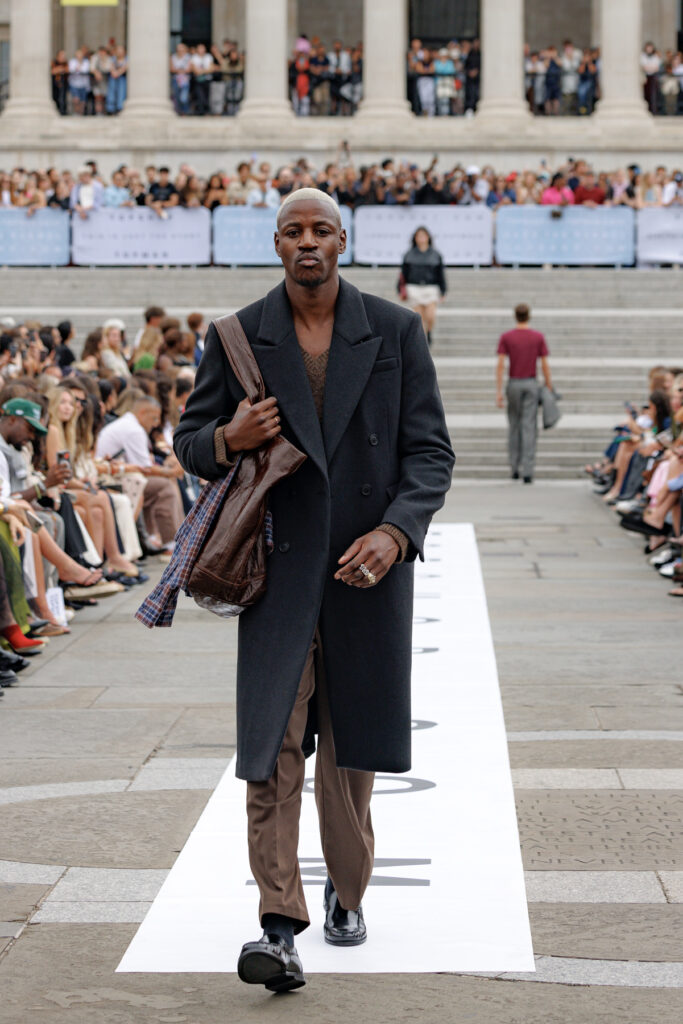 A model wearing a black overcoat and brown leather trousers walks the Topman autumn/winter 2025 show in Trafalgar Square.